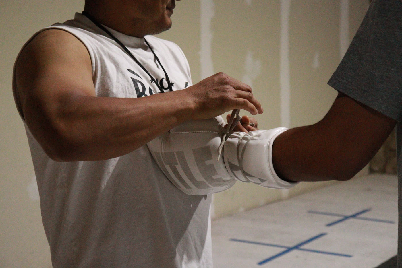 Una persona ajusta una protección de antebrazo a otra antes de entrenar.